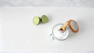 Barattolo di bicarbonato con cucchiaio in legno accanto a due metà di lime su sfondo chiaro