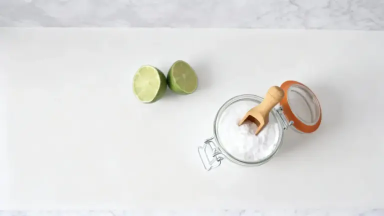 Barattolo di bicarbonato con cucchiaio in legno accanto a due metà di lime su sfondo chiaro
