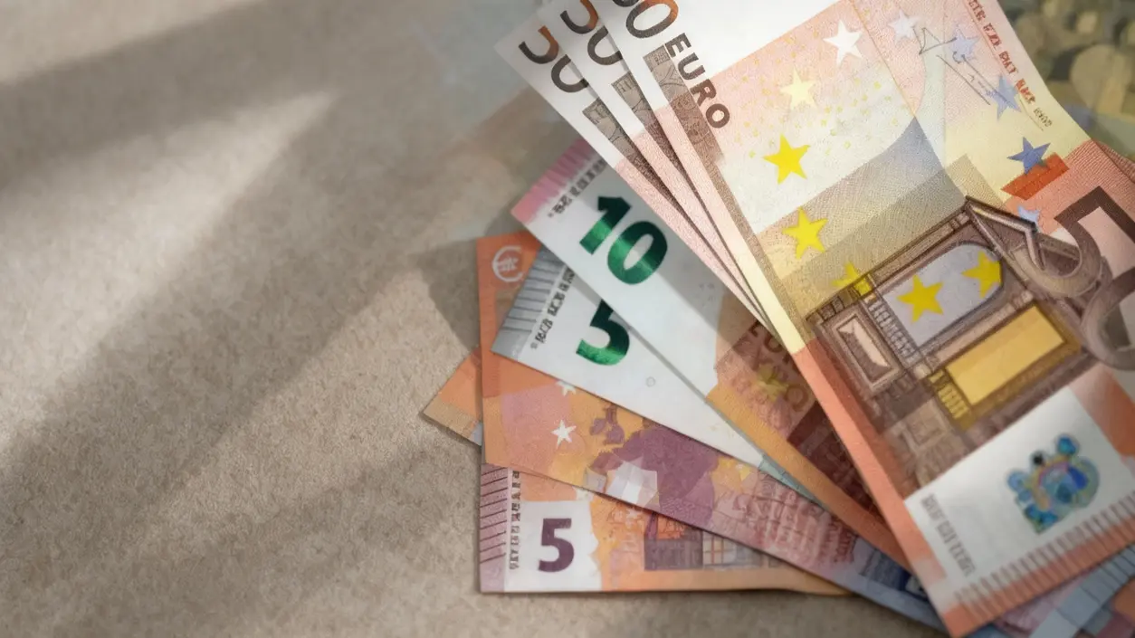 Banconote in euro sparse su un tavolo chiaro, raffiguranti diversi tagli di valuta.