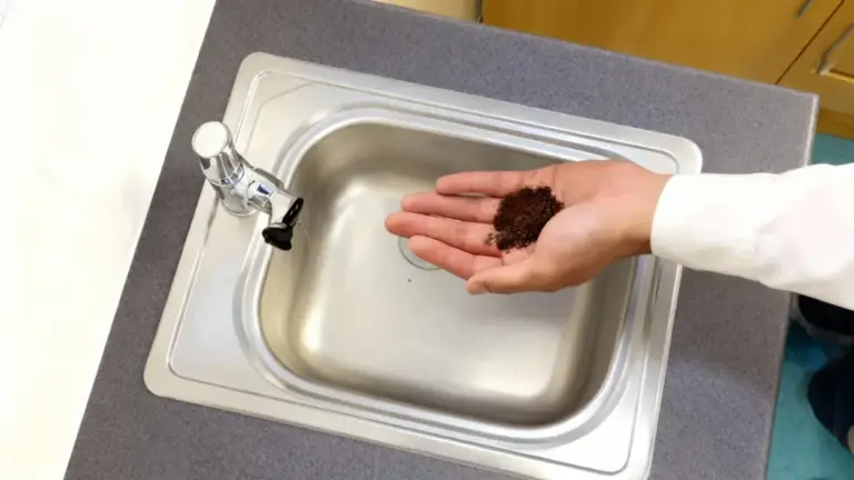 Una mano tiene dei fondi di caffè sopra un lavandino in acciaio inox