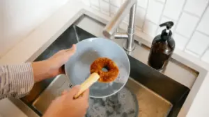Una persona lava un piatto con una spazzola davanti a un lavello da cucina