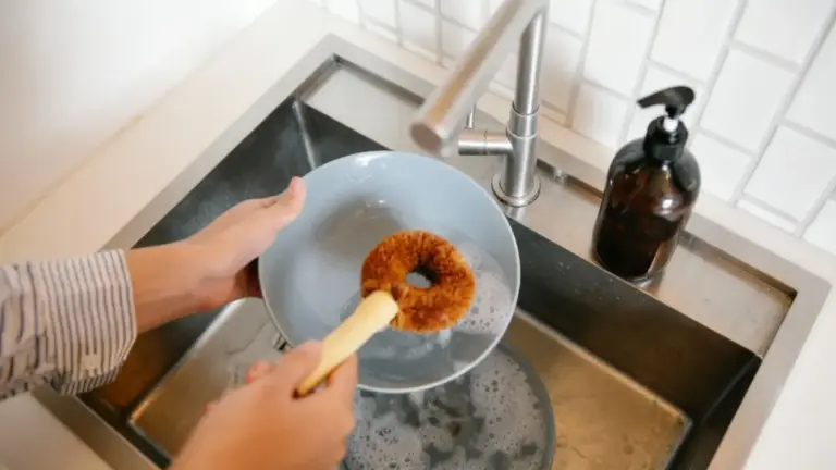 Una persona lava un piatto con una spazzola davanti a un lavello da cucina