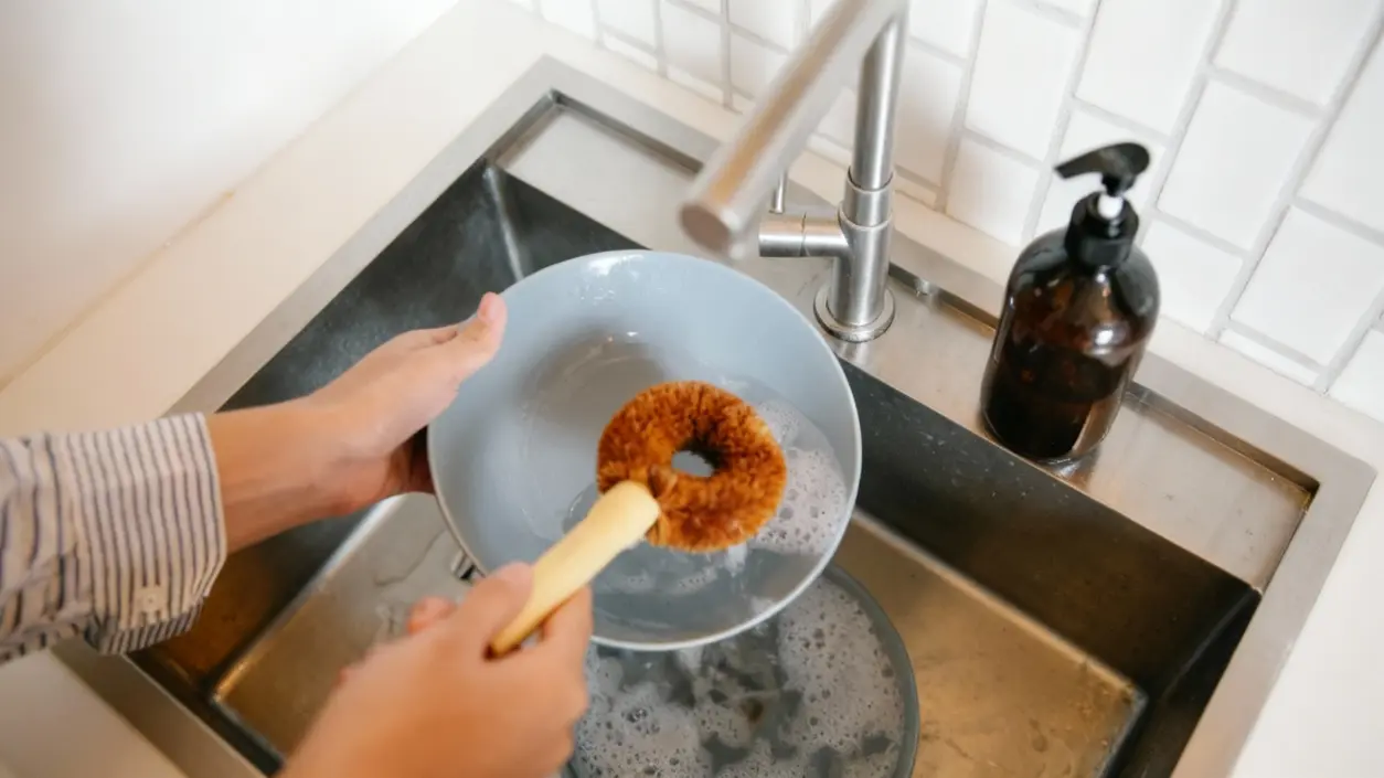 Una persona lava un piatto con una spazzola davanti a un lavello da cucina