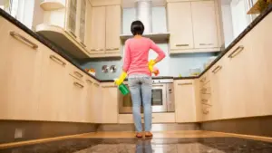 Persona che pulisce sportelli in legno chiaro della cucina con guanti e spray