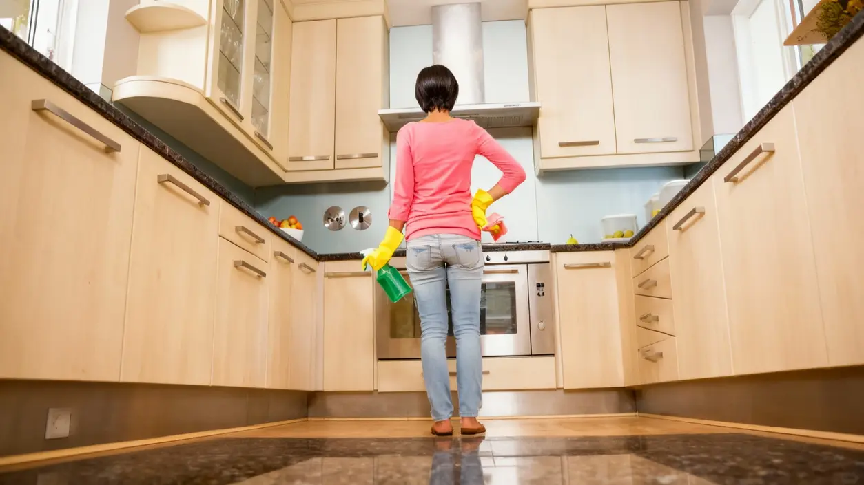 Persona che pulisce sportelli in legno chiaro della cucina con guanti e spray