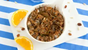 Piatto di sarde a beccafico alla siciliana con arancia e pinoli su tovaglia a righe