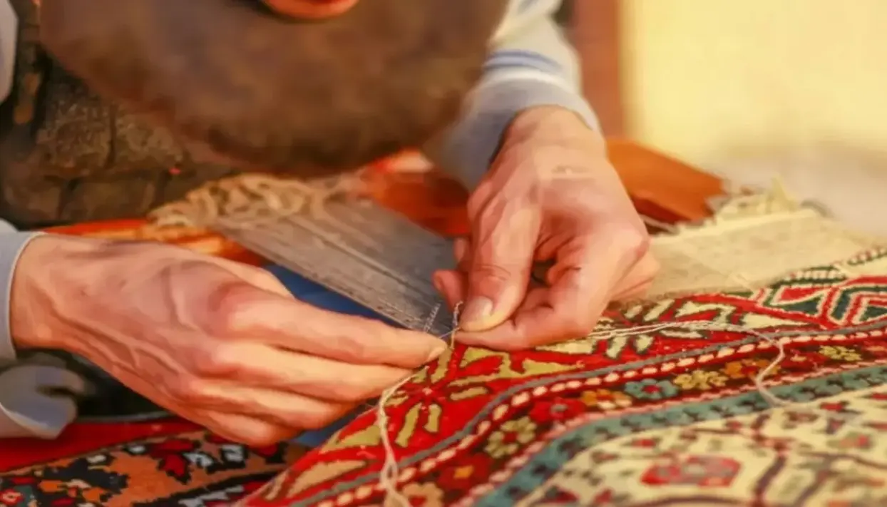 Mani che lavorano alla tessitura di un tappeto persiano con fili colorati