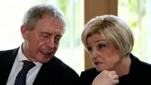 Due persone in abiti formali discutono seriamente in un ambiente interno.