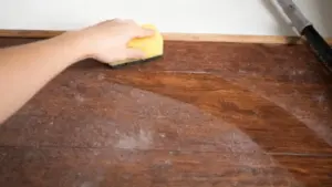 Mano che pulisce la polvere da una superficie in legno con una spugna