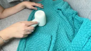 Una persona utilizza un rasoio elettrico per rimuovere pelucchi da un cappotto di lana turchese