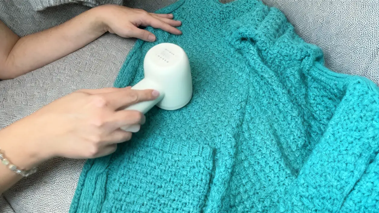 Una persona utilizza un rasoio elettrico per rimuovere pelucchi da un cappotto di lana turchese