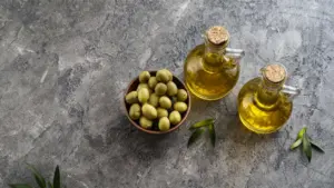 Ciotola di olive verdi accanto a due bottiglie di olio d'oliva su sfondo grigio