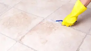 Mano con guanto giallo che pulisce le fughe del pavimento con uno spazzolino