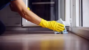 Persona che pulisce un vetro con un panno in microfibra indossando guanti gialli