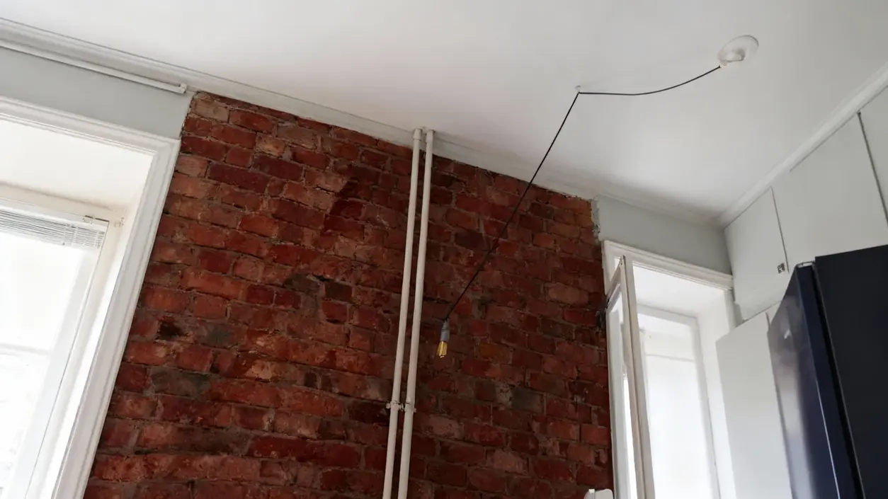 Parete in mattoni a vista con tubature e arredamento minimal in un piccolo appartamento