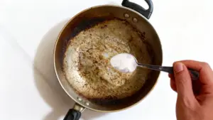 Pentola bruciata con incrostazioni mentre una mano aggiunge del bicarbonato di sodio